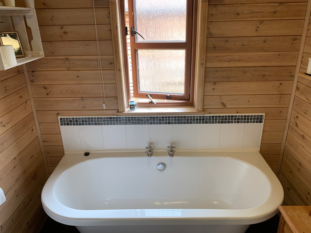 Roll-top bath with mosaic tile surround and frosted window